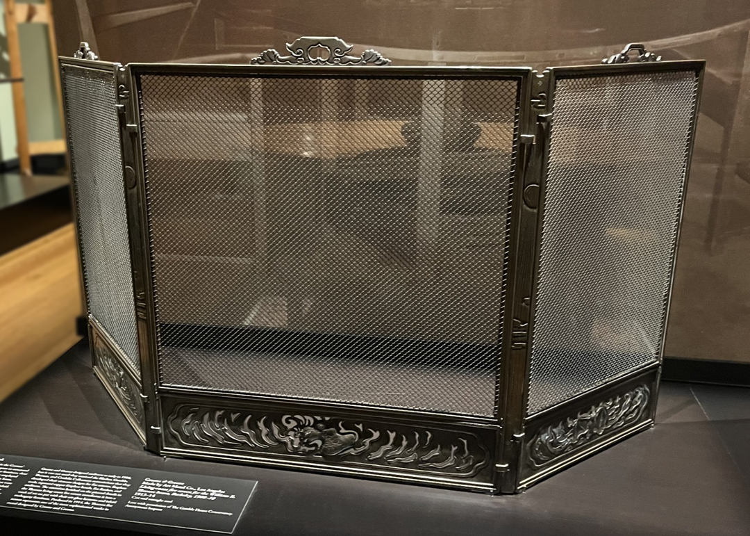 A close-up view of a metal fireplace grate with an ornate border at the bottom.