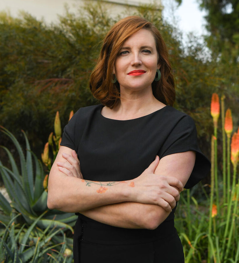 Shannon McHugh stands, arms crossed, in front a garden.