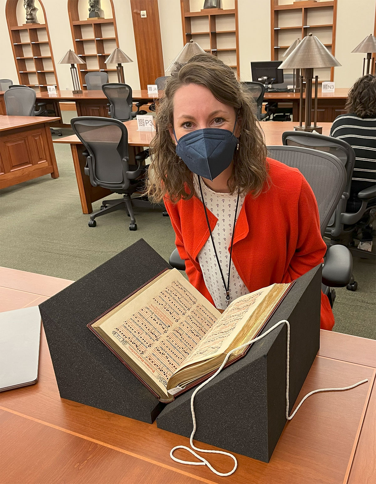 A person in a mask sits in front of a book set on a book rest.