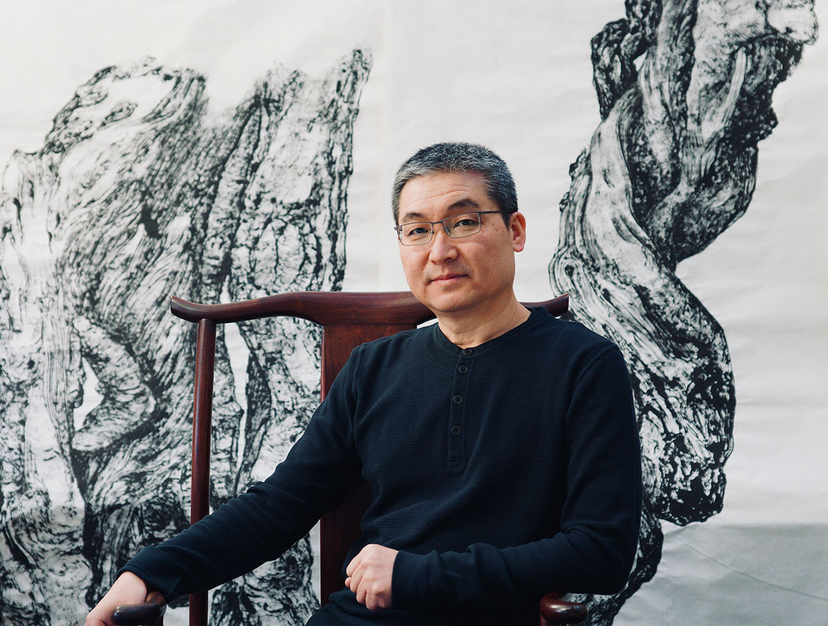 A person sits in a wood chair in front of a wall-sized painting.