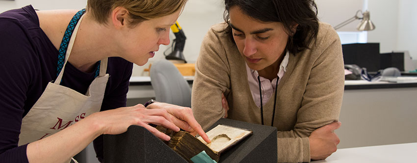 Senior book conservator Andrea Knowlton (left) and Racha Kirakosian, assistant professor of German and the Study of Religion at Harvard University, look at a pear-shaped recess inside the front cover of a 15th-century Dutch codex known as Huntington Manuscript 1048. Photograph by Kate Lain.
