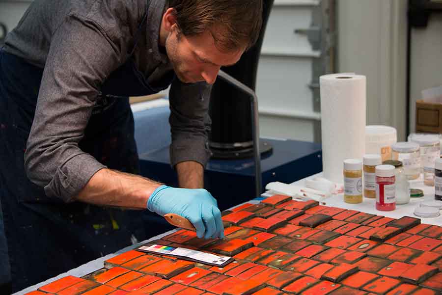 In this photograph, MacLean uses an artist knife to apply a thin coat of a treatment comprising acetone, Paraloid B-72 (a clear acrylic resin), marble powder, and dry pigment to a damaged section of a tile.