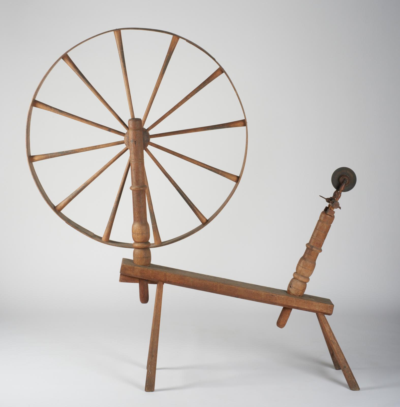 Wooden spinning wheel: large wheel with spokes attached to one end of a simple bench-like structure with a pulley device attached to the other end.  