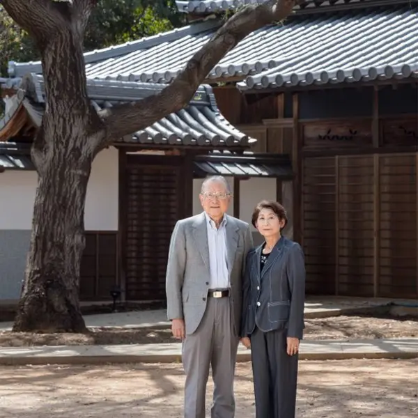A couple stand in front of a partially-built Japanese house.