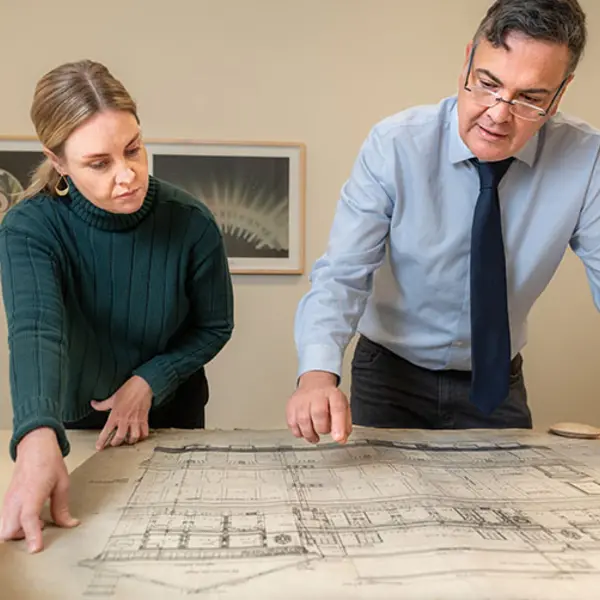 Two people look down at an architectural drawing set on a table.