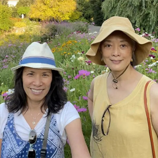 Two people smile at the camera in front of a field of pink and white flowers.