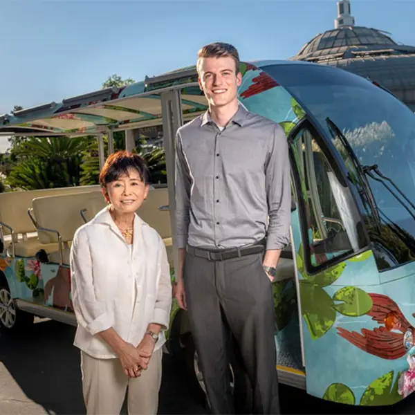 Two people stand in front of an electric passenger vehicle that's wrapped in a koi-inspired design.
