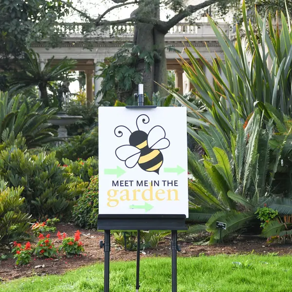 A sign in a garden that says, “Meet Me in the Garden.”