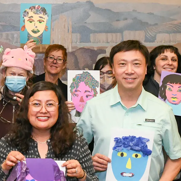 A group of adults stands with self-portraits made from cut paper.