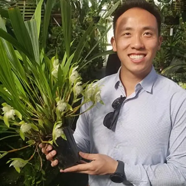 A smiling person holds a potted orchid.