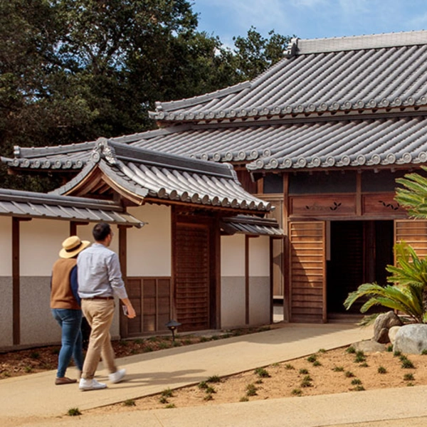 Two people walk toward the entrance to a traditional Japanese home.