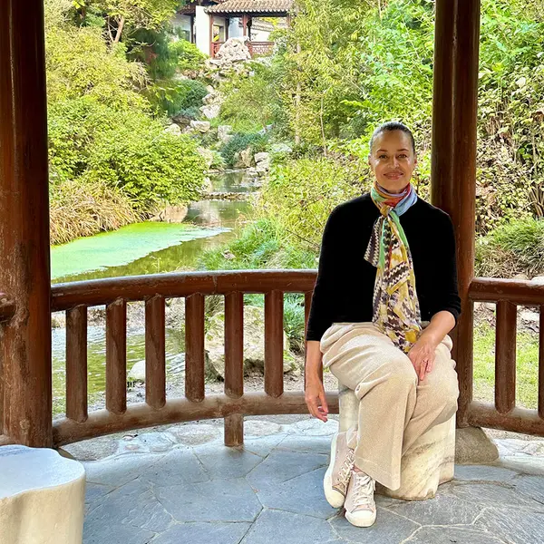 A person sits in a wooden pavilion with a stream in the background.