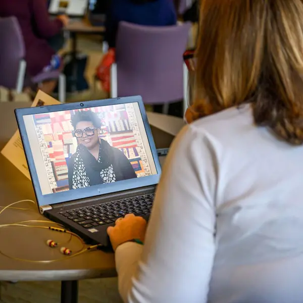 A person sits at a laptop, looking at an image of a person in a gallery.