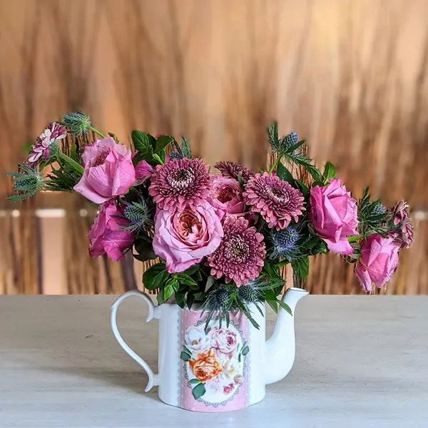 An arrangement of pink flowers in a decorated teapot vase.