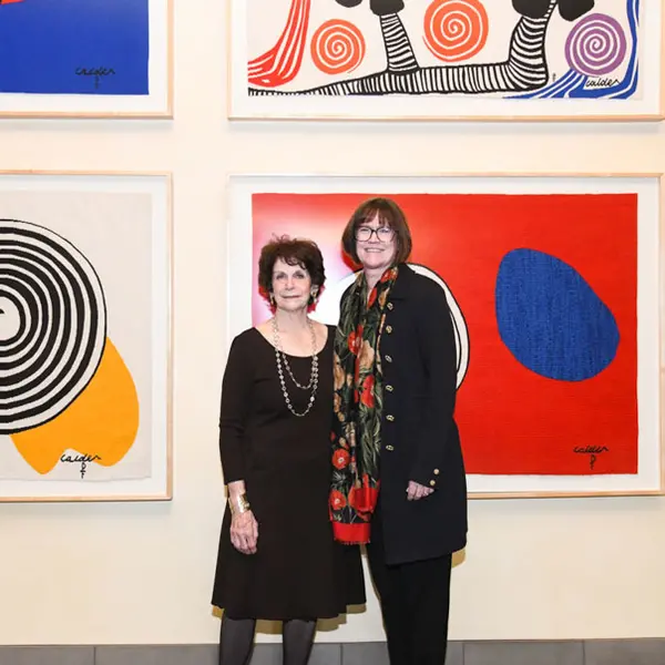 Two people stand together in front of a wall of framed artwork.
