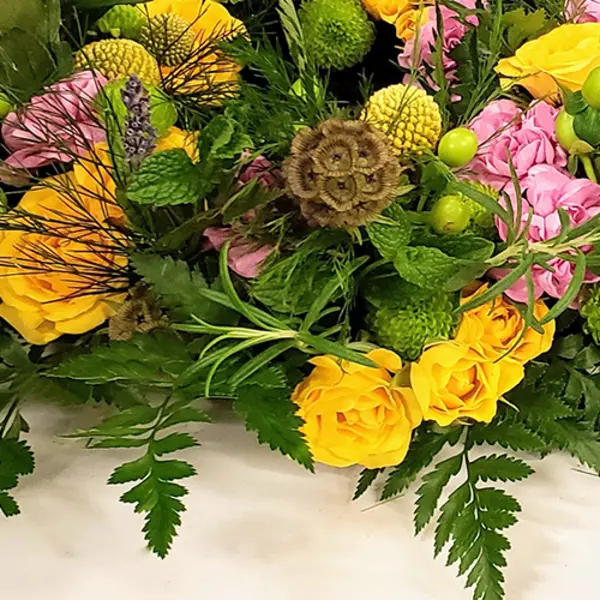 A floral arrangement with yellow and pink roses and green herbs.