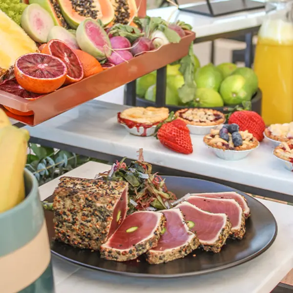 A buffet spread with seared meat, fresh fruit, desserts, and juice.