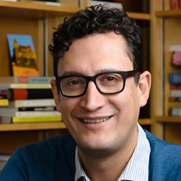 Pablo F. Gómez poses for headshot taken in front a bookshelf.