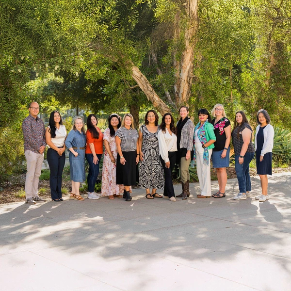 A group of people pose in a row, standing in a garden.