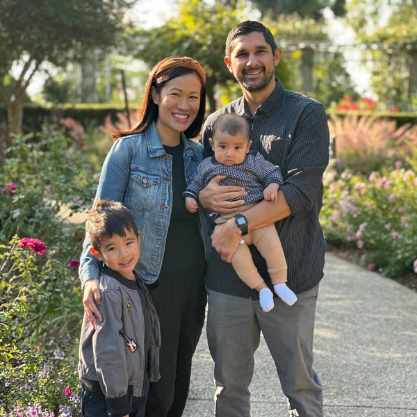 Two parents stand with their young children in a garden.