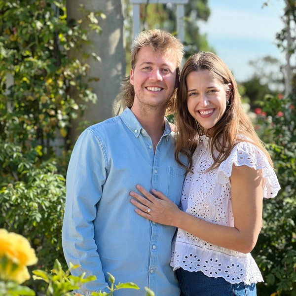 A smiling couple stands in a green garden.