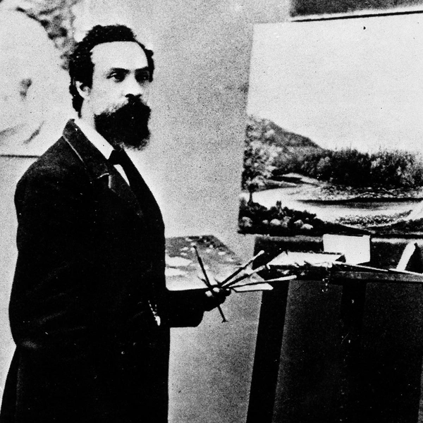 A black-and-white photo of a man in a suit, holding a palette and brushes in front of an easel.