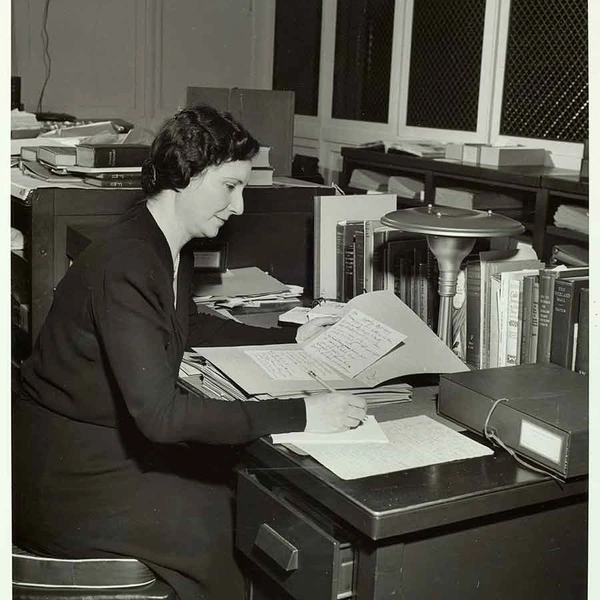 A black and white photo of a person at a desk with papers.