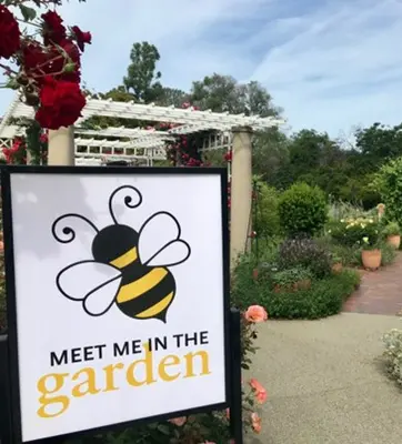 garden with a sign that reads "Meet Me in the Garden" with a bee on it