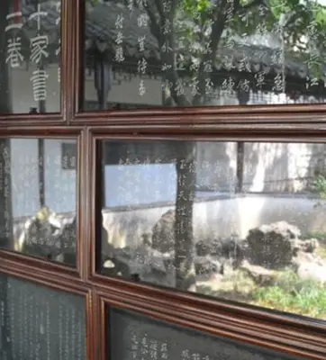 A collection of stone slabs with Chinese writing are framed in dark wood on a wall. A wall and roof are reflected on the glass that covers the slabs.