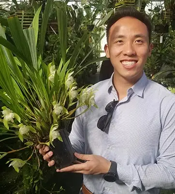 A smiling person holds a potted orchid.