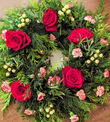 A wreath made of evergreen foliage, roses, carnations, and herbs.