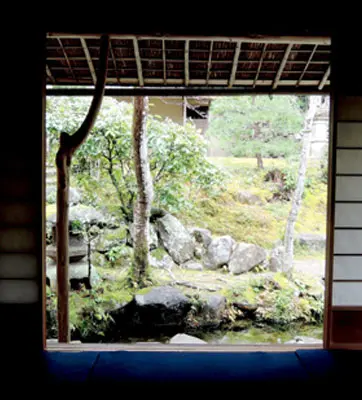 A small hill with trees and rocks viewed from the open doorway of a traditional Japanese tearoom.