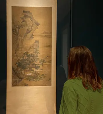 A person in a gallery looks at a painting on a scroll.