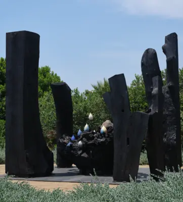 A large sculpture in a garden, created with charred wood and ceramics.