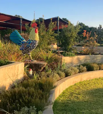 A large statue of a rooster with colorful mosaic in a garden.