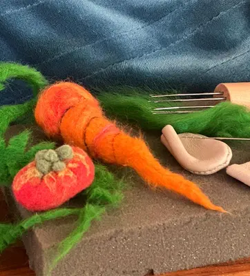 A carrot, tomato, and leaves made from colorful felt.
