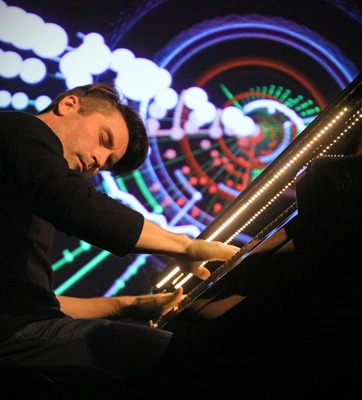 A musician sits at a lit piano.