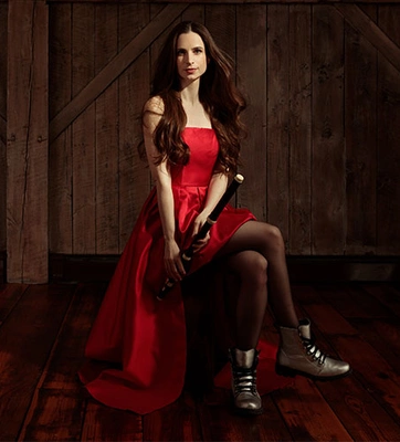 A musician in a red dress holds a flute at their side.