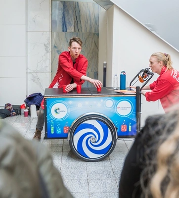 Two people in red coats running a science experiment in front of a crowd.