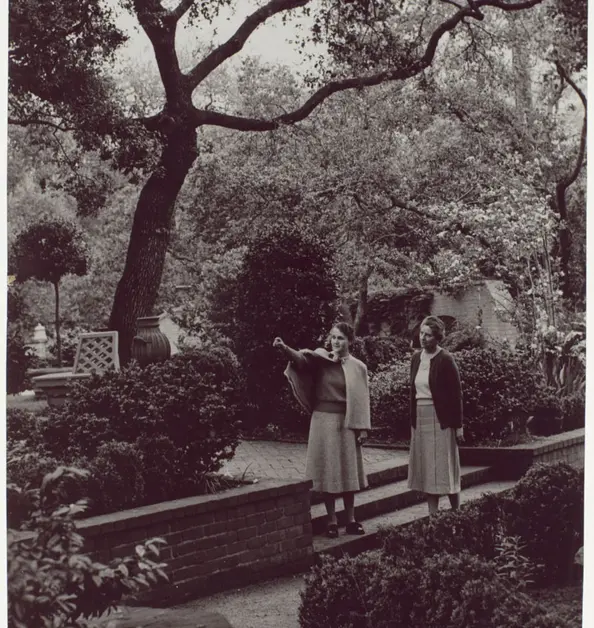 A grayscale photo of two people in a mature garden.