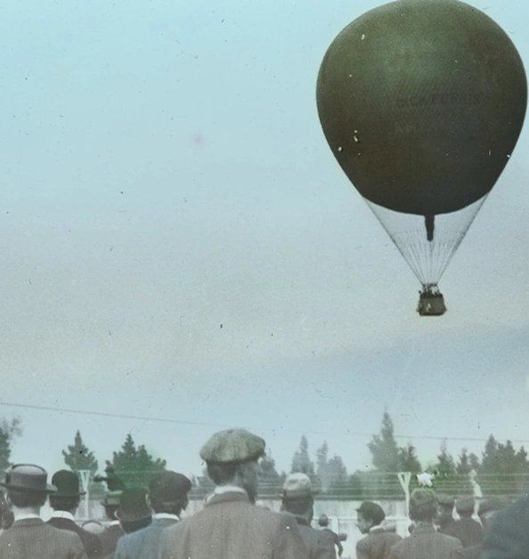 A crowd watches a hot air balloon in the sky.