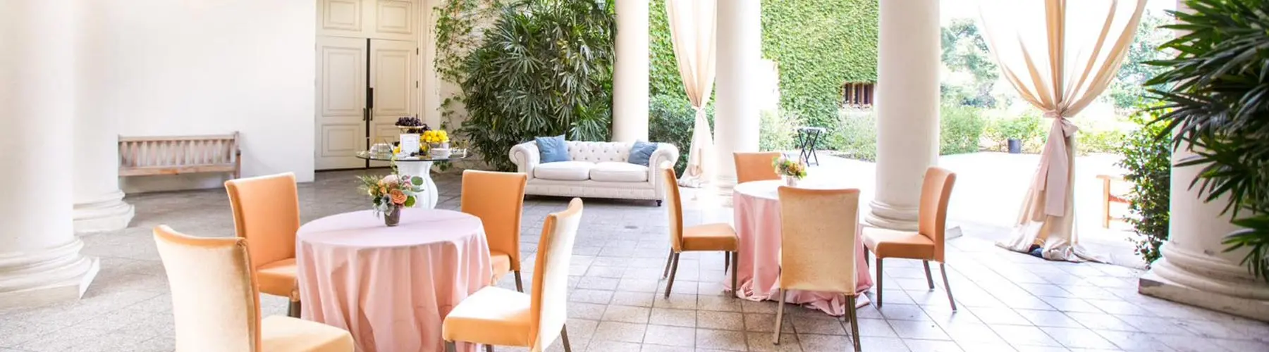 Light peach tableclothes and tan chairs fill an outdoor loggia.