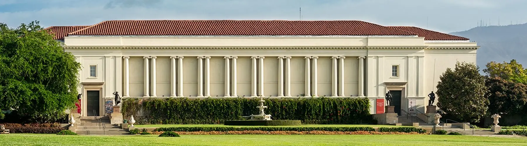 A white building with numerous pillars and a spanish tile roof with a green lawn in front.