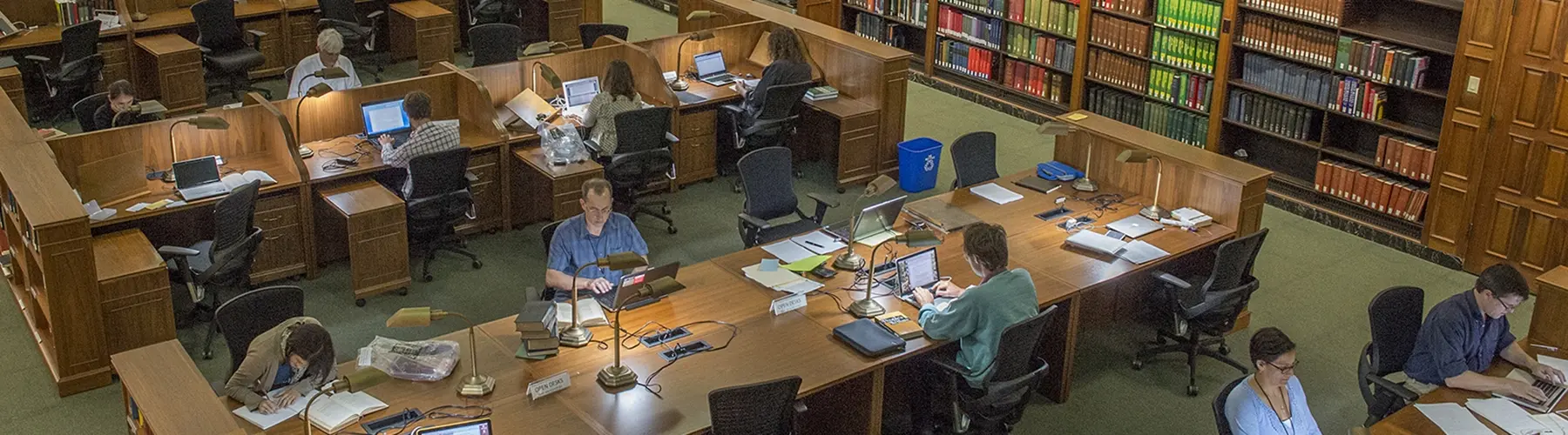 A view from above of people sitting at tables and reading in a library with books all around.