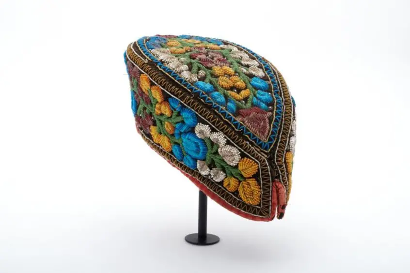 Black velvet cap in the shape of a pointed oval, with beadwork in blue, white, green, yellow, and red forming flowers and stems all over; made by a Haudenosaunee woman. 