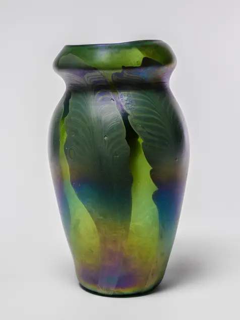 Green vase against a white background. Two large green leaves are visible on the vase. The leaves appear darker than the background. Light reflects off the lower half of the vase.