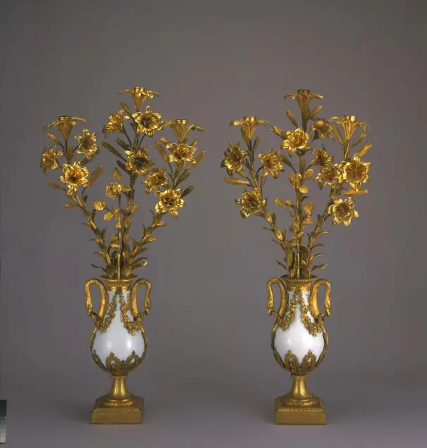 Two similar candelabra. Each candelabrum has a white and gold base and twelve gold candle-holders in the shape of lily flowers.