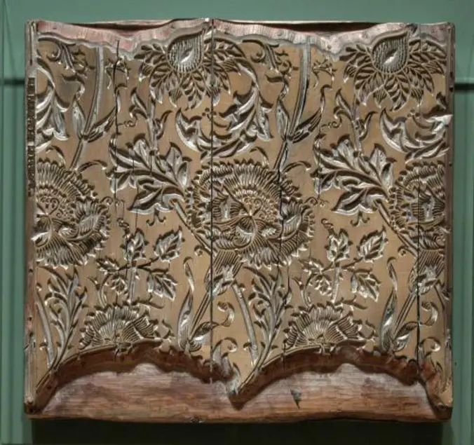 Square woodblock with stylized plant parts carved into it.