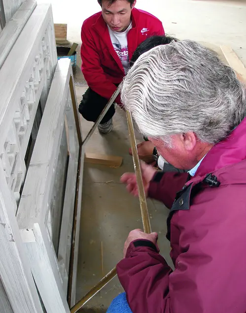 Two people examine a wooden rectangle connected to a rectangular stone carving 