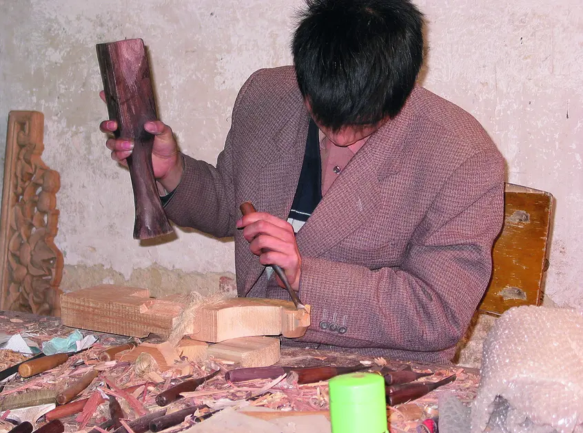 Person working at a table with hand tools. The tools appear to be made of wood, as does the object the person is working on.